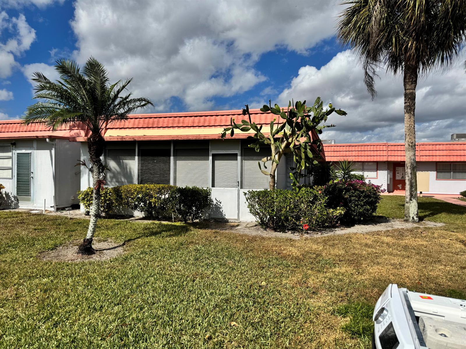 A single-story residential building with a salmon-colored roof, palm trees, and a cactus — 277 Seville L, Delray Beach FL 33446, DELRAY BEACH, FL