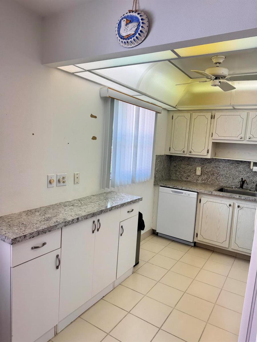 A kitchen features white cabinets, granite countertops, a white dishwasher, and a tiled floor — 277 Seville L, Delray Beach FL 33446, DELRAY BEACH, FL