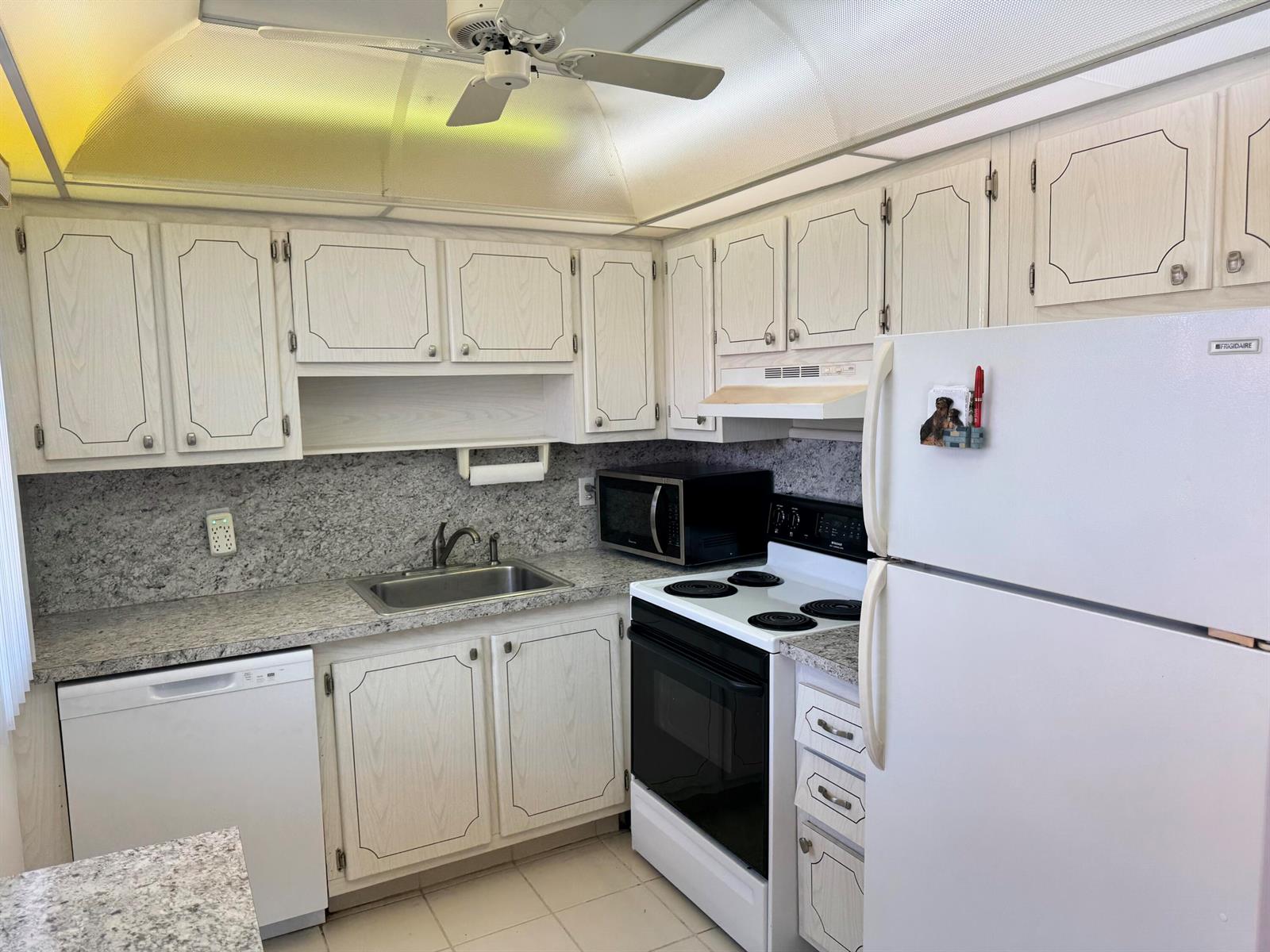 A kitchen with white cabinets, speckled granite countertops, a white stove, and a white refrigerator — 277 Seville L, Delray Beach FL 33446, DELRAY BEACH, FL