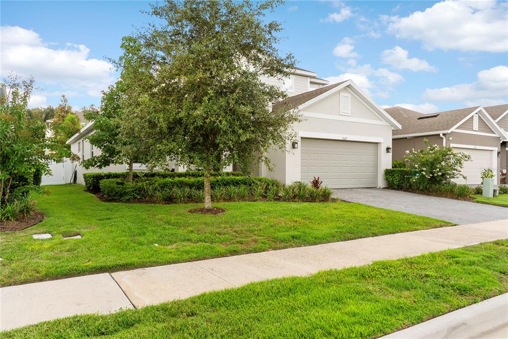 A light-colored suburban house with a two-car garage, a paved driveway, and a front lawn — 2527 NATOMA BOULEVARD, MOUNT DORA, FL