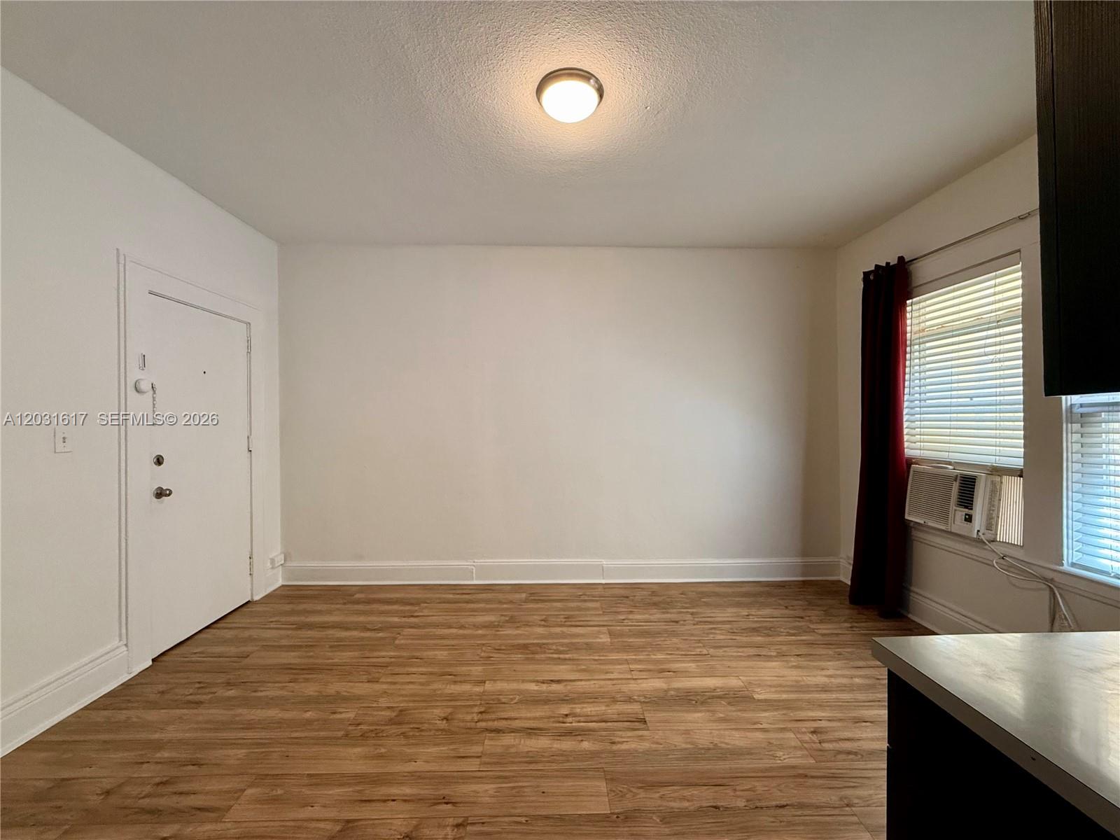 An empty room features wood-look flooring, white walls, a ceiling light, and a window unit — 126 Mendoza Ave # 2A, Coral Gables FL 33134, CORAL GABLES, FL