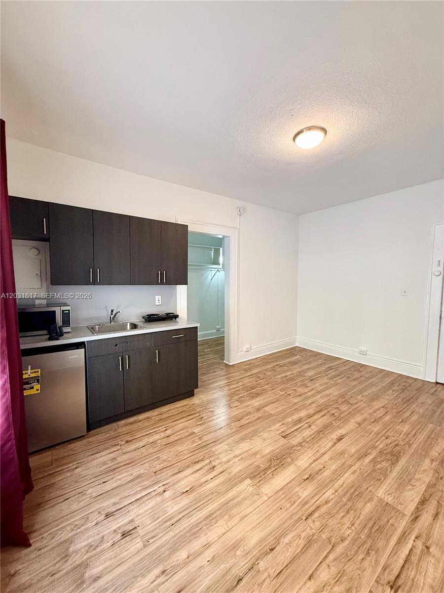 A small kitchen area with dark cabinets and wood-look flooring opens into an adjacent room — 126 Mendoza Ave # 2A, Coral Gables FL 33134, CORAL GABLES, FL