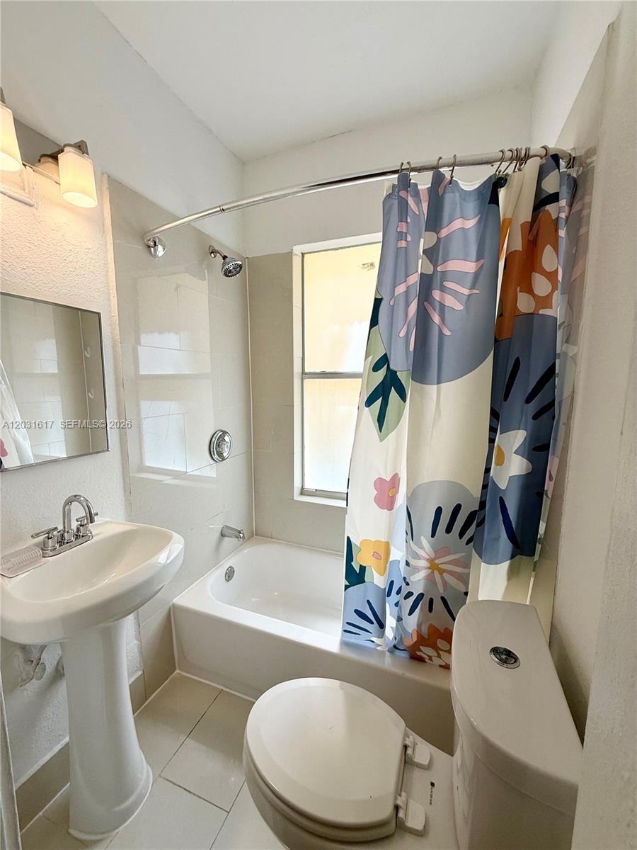 A bathroom features a pedestal sink, a toilet, and a bathtub with a floral shower curtain — 126 Mendoza Ave # 2A, Coral Gables FL 33134, CORAL GABLES, FL