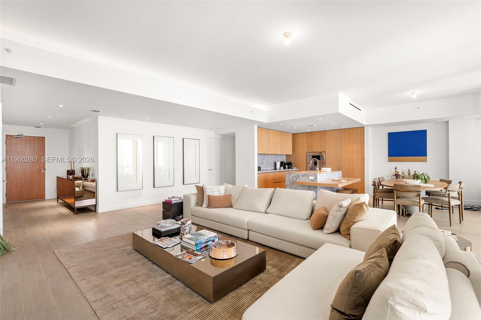 A modern living room features a large sectional sofa, circular mirror, and open kitchen area — 500 Alton # 2203, Miami Beach FL 33139, MIAMI BEACH, FL