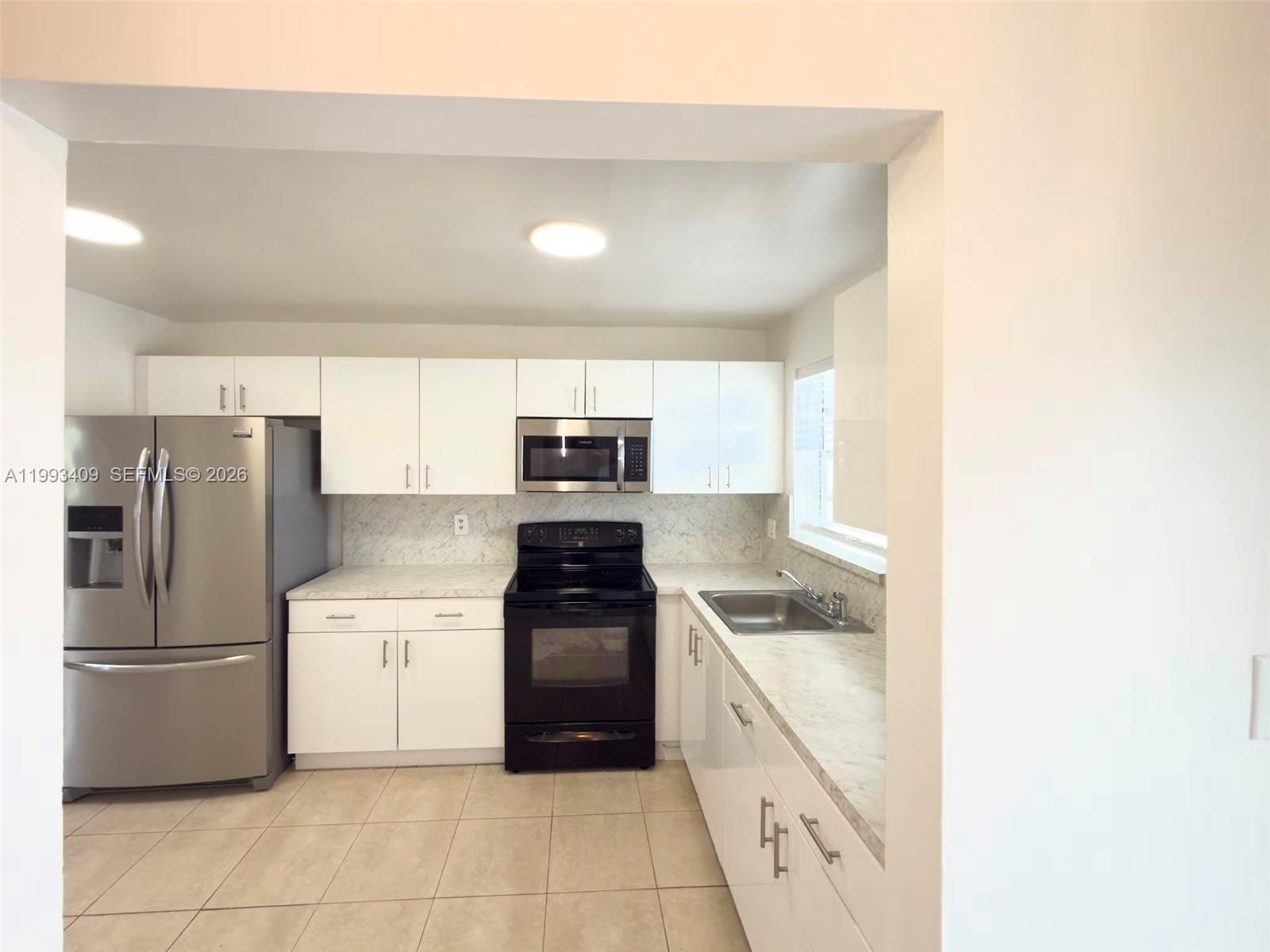 A kitchen features white cabinets, stainless steel appliances, a black stove, and marble-look countertops — 609 S State Road 7 # 1C, Margate FL 33068, MARGATE, FL