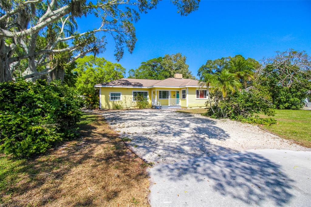 A yellow single-story house with a gravel driveway and a large tree in the foreground — 5812 7TH AVENUE NW, BRADENTON, FL