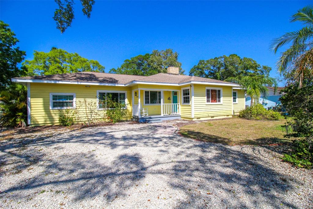 A yellow, single-story house with horizontal siding features a gravel driveway and a front porch — 5812 7TH AVENUE NW, BRADENTON, FL