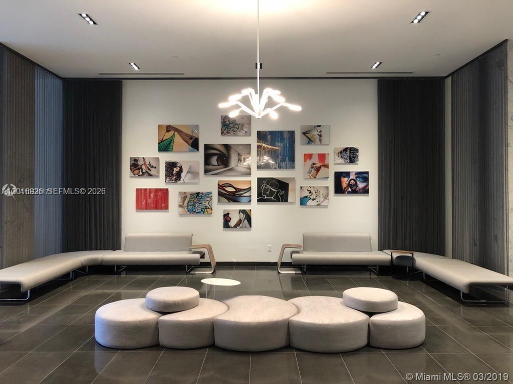 A modern lobby features a gallery wall of art, gray modular seating, and a chandelier — 1600 NE 1st Ave # 3614, Miami FL 33132, MIAMI, FL