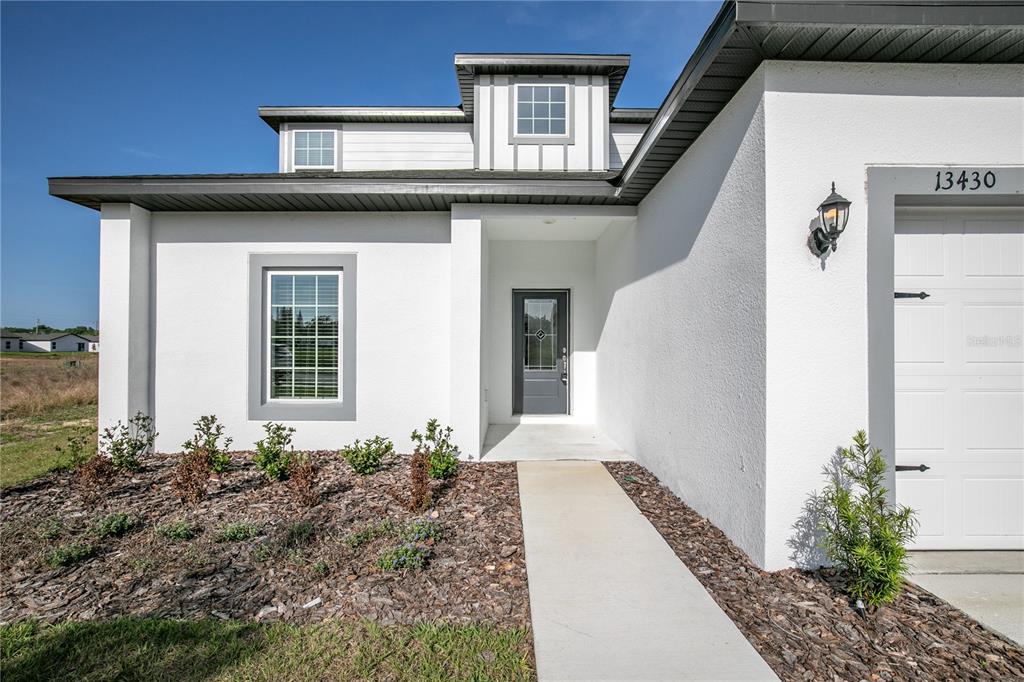 The exterior of a white house features a front door, a garage, and a walkway — 13430 LEAPING WATER WAY, ASTATULA, FL