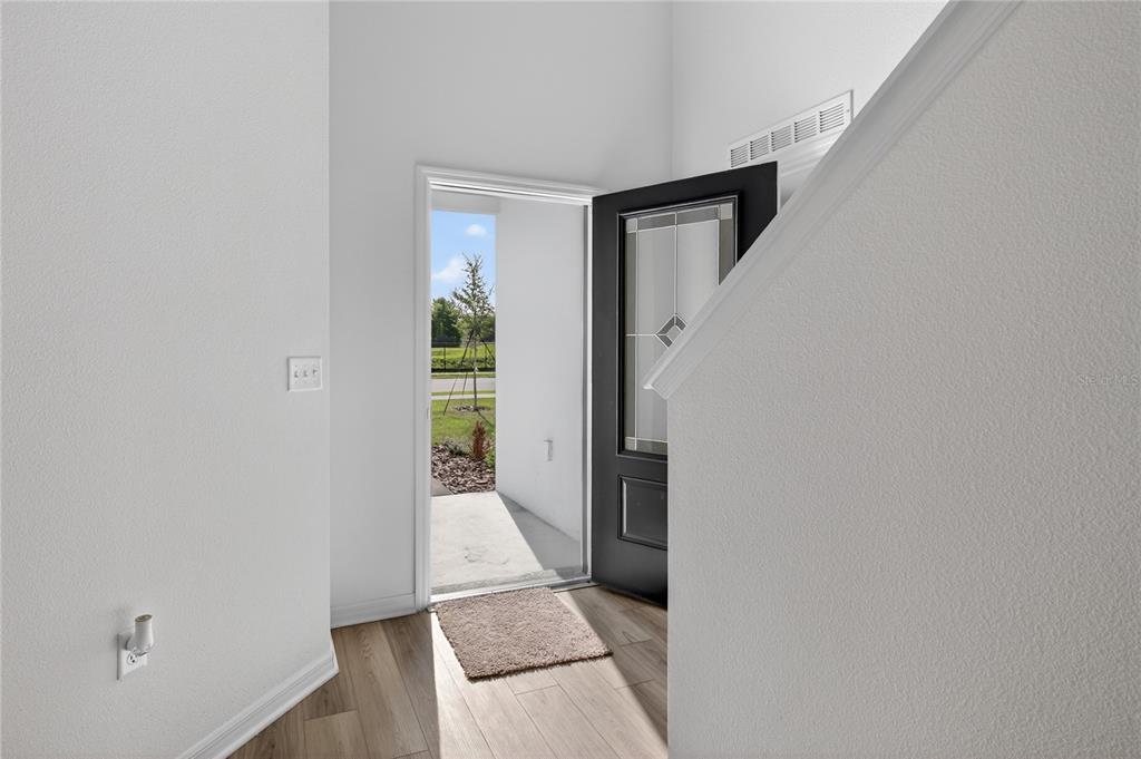 An entryway with light wood-look flooring, white walls, and an open black front door — 13430 LEAPING WATER WAY, ASTATULA, FL