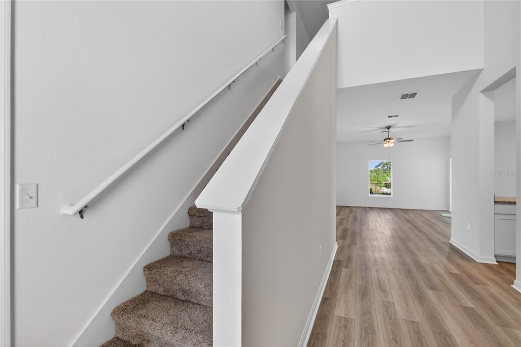 A carpeted staircase with a white handrail sits next to a room with wood flooring — 13430 LEAPING WATER WAY, ASTATULA, FL