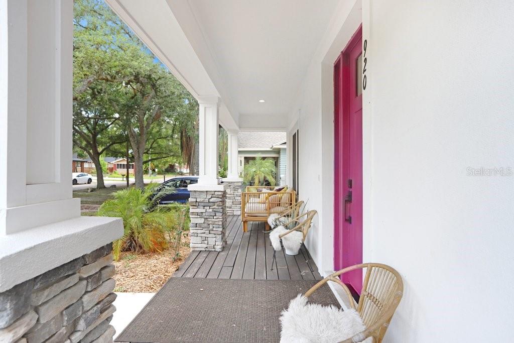 A covered front porch features a bright pink door, stone-based columns, and outdoor seating — 920 E SHADOWLAWN AVENUE, TAMPA, FL
