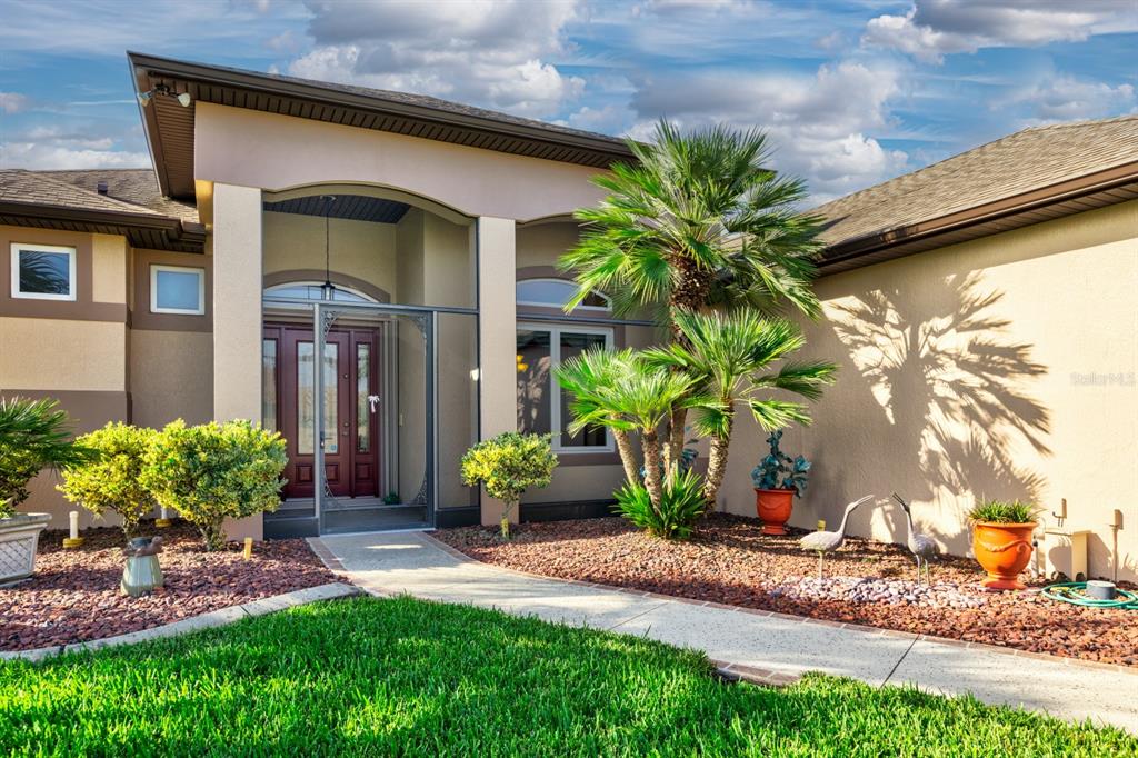 The exterior of a house features a covered entryway, a palm tree, and landscaped beds — 5530 CELEBRATION WAY, LEESBURG, FL