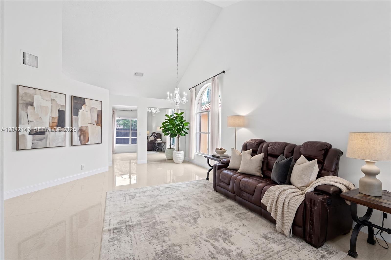 A living room features a brown leather sofa, a chandelier, and light-colored tile flooring — 2722 Cayenne Ave, Cooper City FL 33026, COOPER CITY, FL