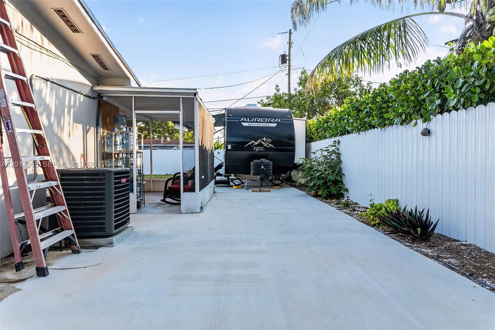 A concrete driveway features a parked travel trailer, a screened-in patio, and a white fence — 9760 Memorial Rd, Cutler Bay FL 33157, CUTLER BAY, FL