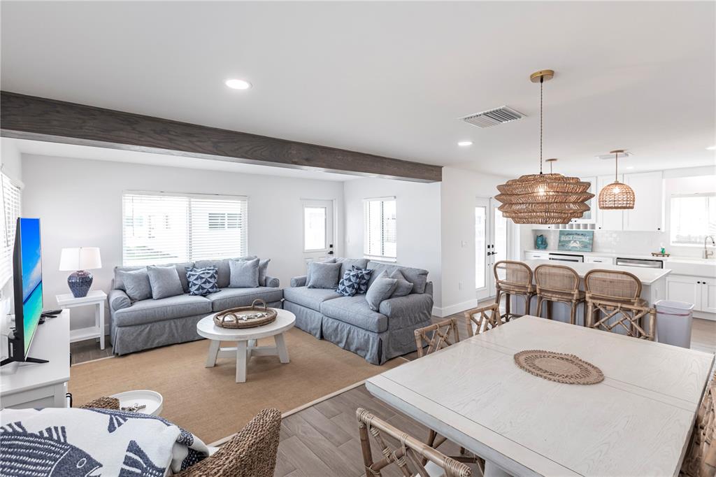An open-concept living and dining area features gray sofas, a wooden beam, and rattan lighting — 6020 MIDNIGHT PASS ROAD UNIT 27, SARASOTA, FL