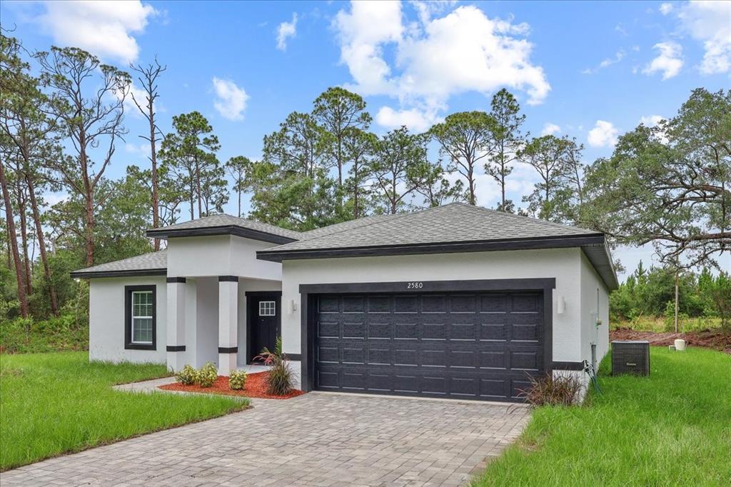A single-story house with a white stucco exterior, black trim, and a paved driveway — 2580 PLUMOSA DRIVE, INDIAN LAKE ESTATES, FL