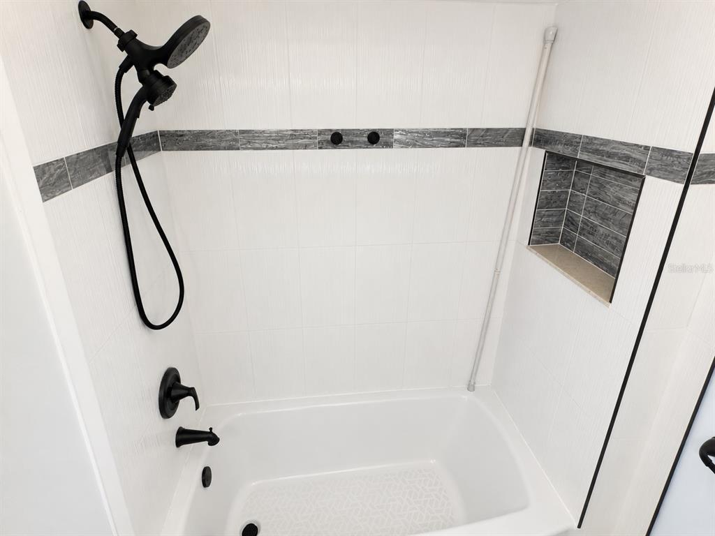A white tiled bathtub and shower enclosure features black fixtures and a recessed wall niche — 1068 LOTUS PARKWAY UNIT 815, ALTAMONTE SPRINGS, FL