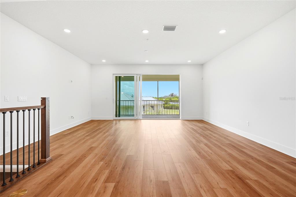 An empty room with wood-look flooring, white walls, recessed lighting, and a sliding glass door — 9936 KEY HAVEN ROAD, SEMINOLE, FL