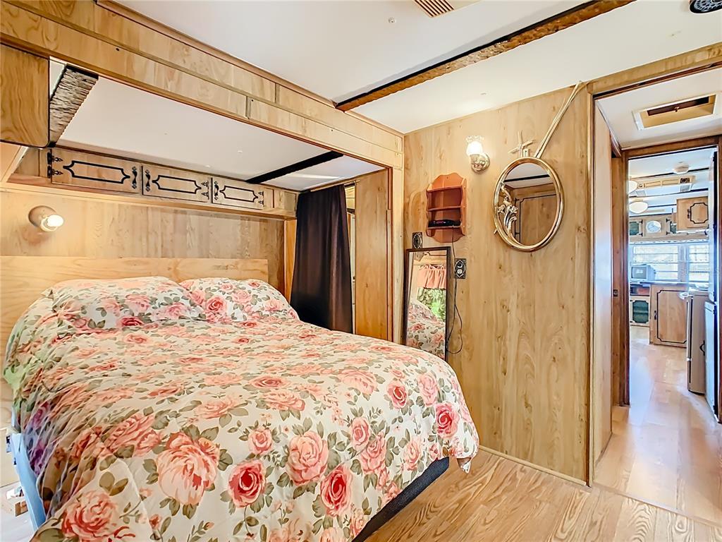 A bedroom with wood-paneled walls, a floral bedspread, and a doorway leading to a kitchen — 9000 US HWY 192 UNIT 407, CLERMONT, FL