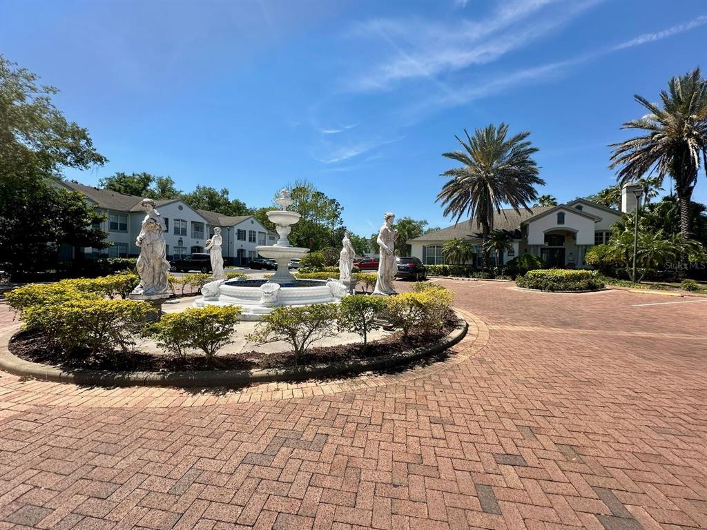 A tiered stone fountain surrounded by statues sits in a brick-paved courtyard near apartment buildings — 4332 S KIRKMAN ROAD UNIT 1004, ORLANDO, FL