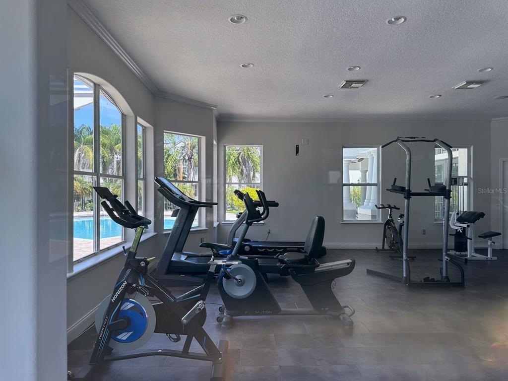 A home gym features exercise equipment, tile flooring, and large windows overlooking a swimming pool — 4332 S KIRKMAN ROAD UNIT 1004, ORLANDO, FL