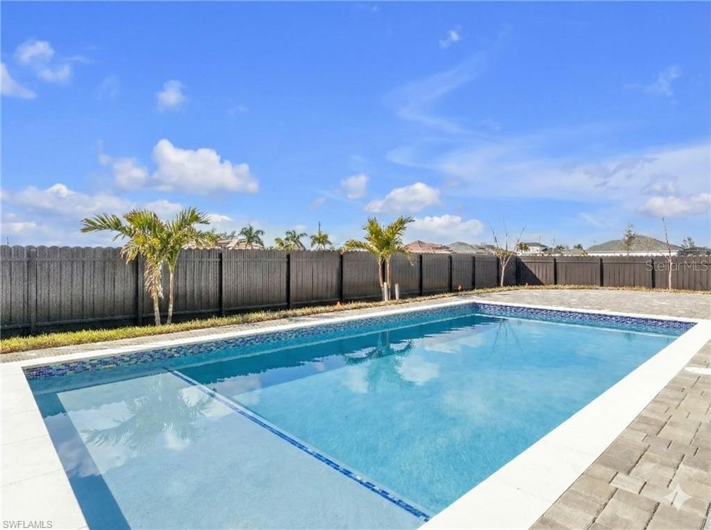 A rectangular swimming pool with a tanning ledge sits in a backyard with a fence — 1015 NW 23RD AVENUE, CAPE CORAL, FL