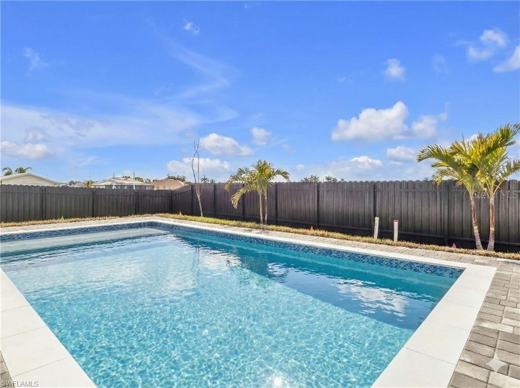 A rectangular swimming pool sits in a backyard enclosed by a dark wooden fence — 1015 NW 23RD AVENUE, CAPE CORAL, FL