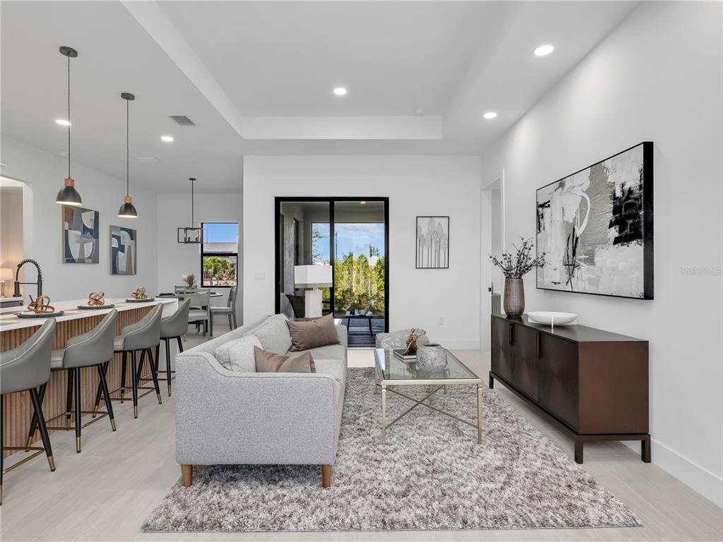 A modern open-concept living room and kitchen featuring gray furniture, wood accents, and sliding doors — 1015 NW 23RD AVENUE, CAPE CORAL, FL