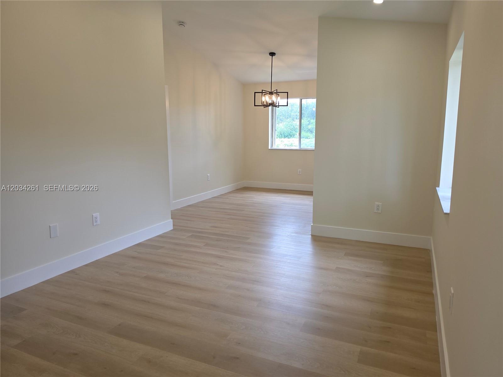 An empty room with light wood-look flooring, beige walls, and a modern hanging light fixture — 13318 SW 152nd St # 3202, Miami FL 33177, MIAMI, FL