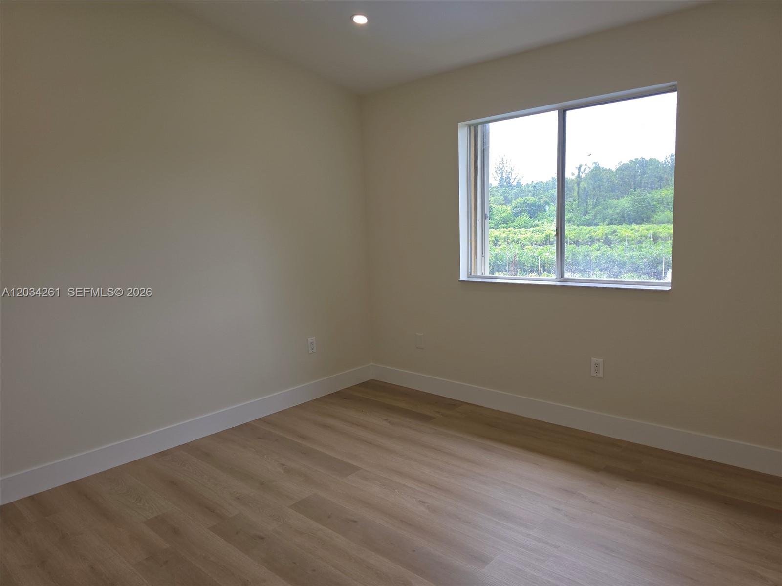 An empty room features light-colored walls, wood-look flooring, and a window overlooking greenery — 13318 SW 152nd St # 3202, Miami FL 33177, MIAMI, FL