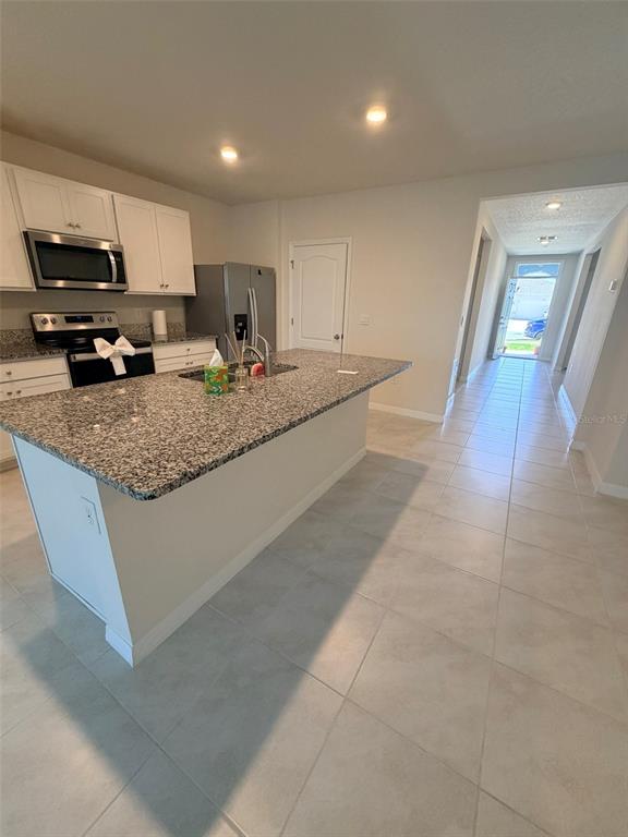 A kitchen features a granite-topped island, white cabinetry, stainless steel appliances, and light tile flooring — 430 TANIS AVENUE, ST CLOUD, FL
