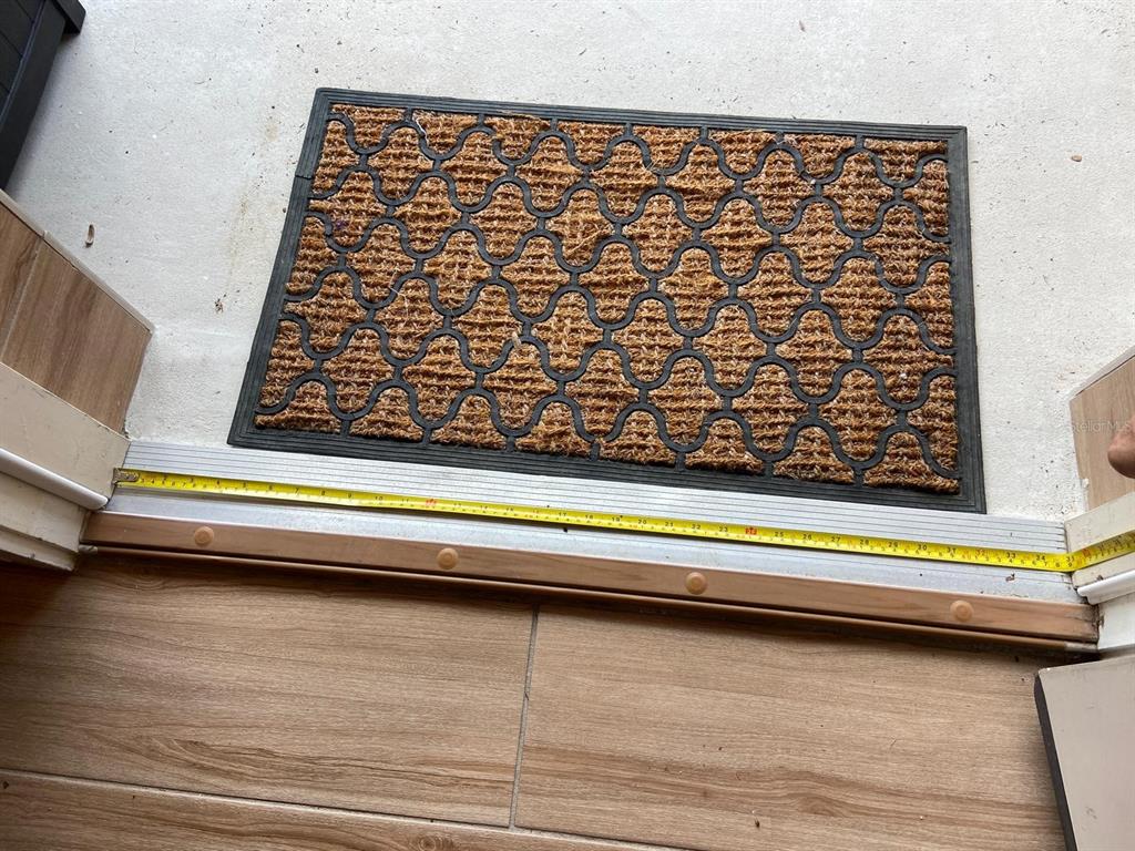 A tape measure lies across a doorway threshold next to a patterned outdoor welcome mat — 7582 BROOKLYN DRIVE, KISSIMMEE, FL