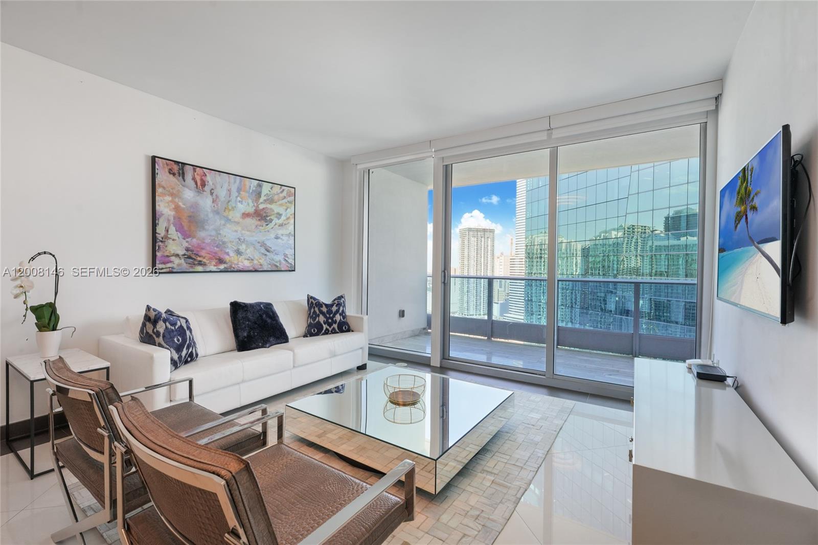 A modern living room features a white sofa, mirrored coffee table, and floor-to-ceiling balcony windows — 200 Biscayne Boulevard Way # 3613, Miami FL 33131, MIAMI, FL