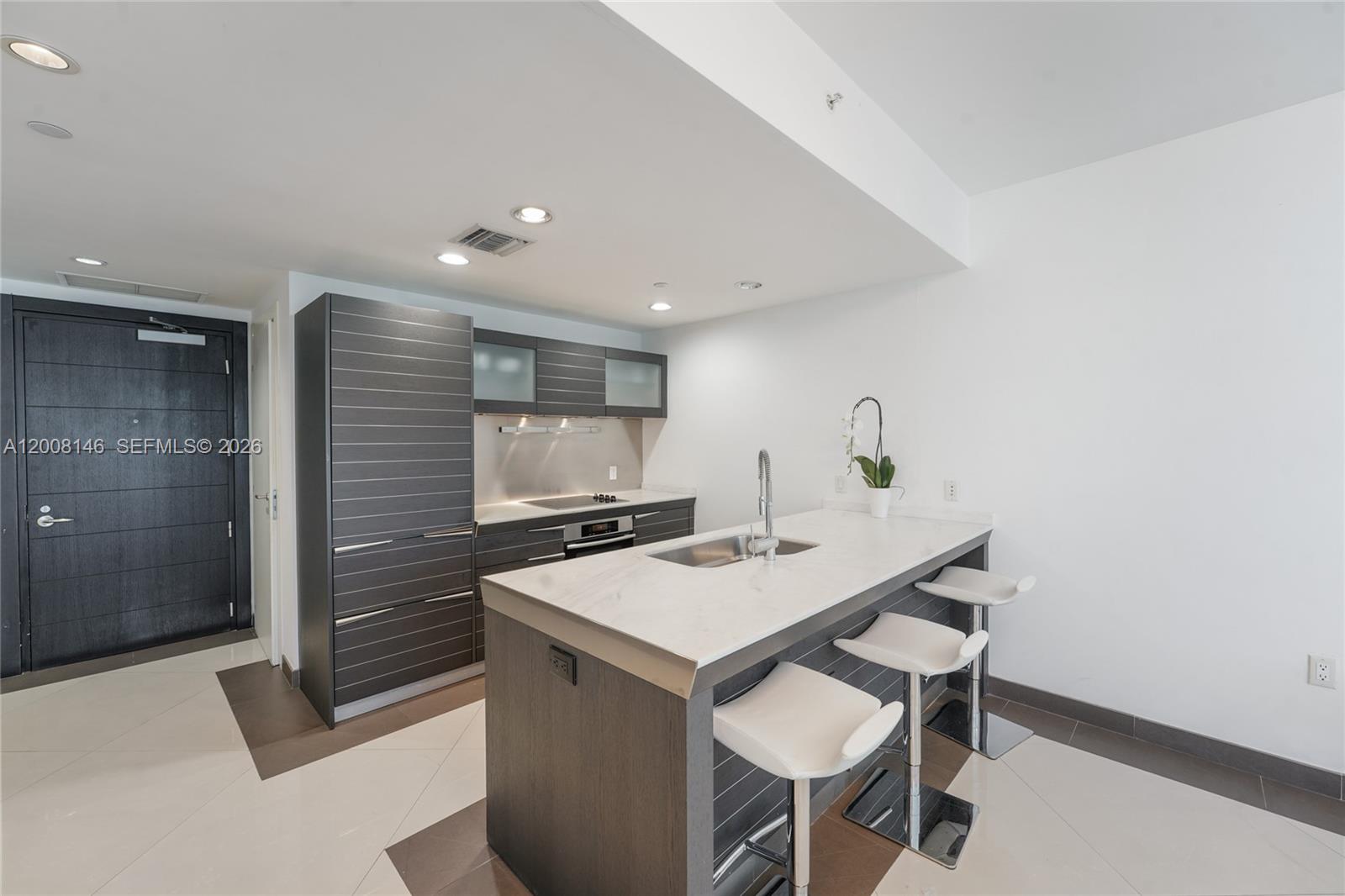 A modern kitchen features dark cabinetry, a white marble island, and three white bar stools — 200 Biscayne Boulevard Way # 3613, Miami FL 33131, MIAMI, FL