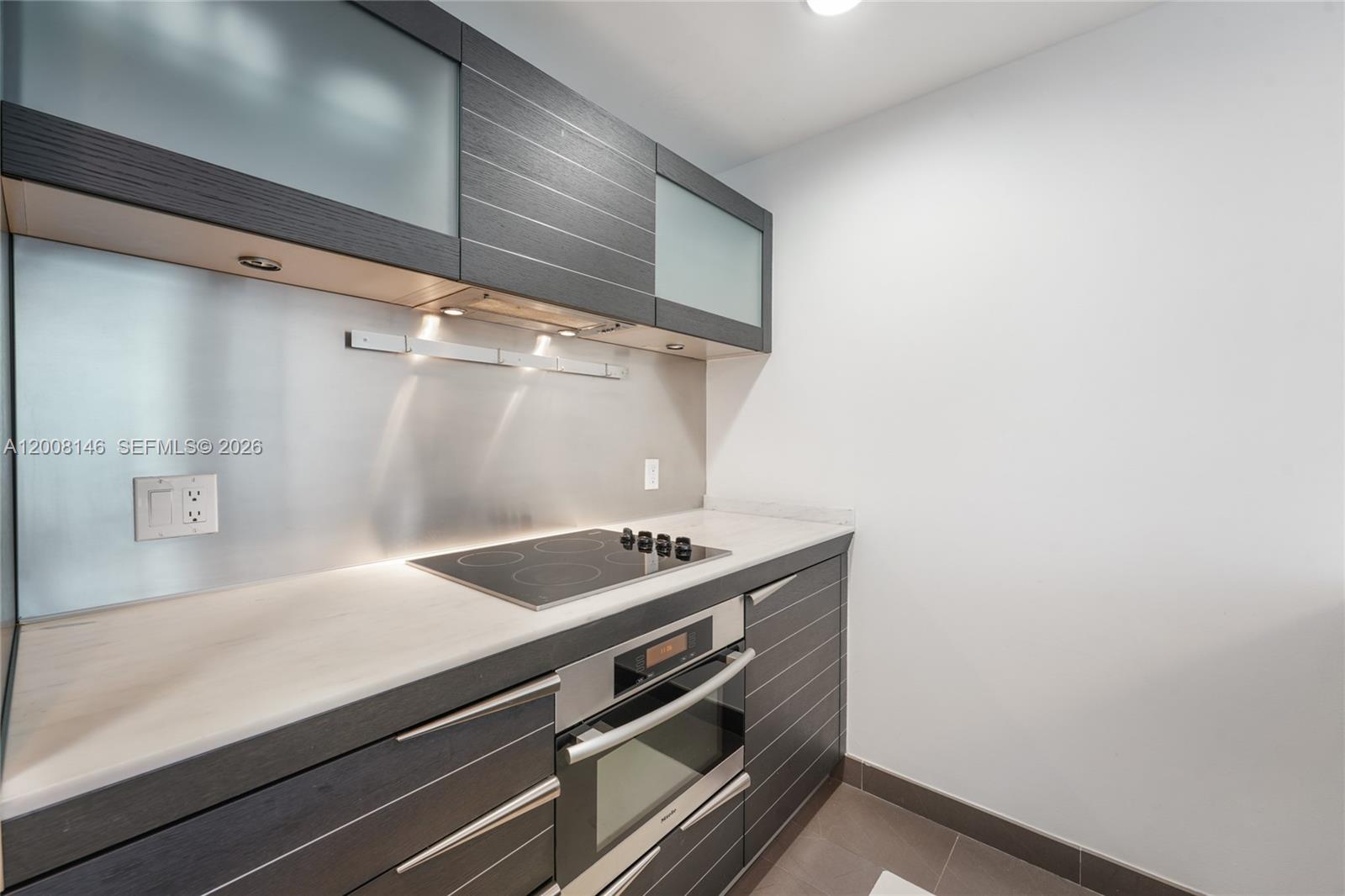 A modern kitchen features dark wood cabinetry, a stainless steel backsplash, and a built-in cooktop — 200 Biscayne Boulevard Way # 3613, Miami FL 33131, MIAMI, FL