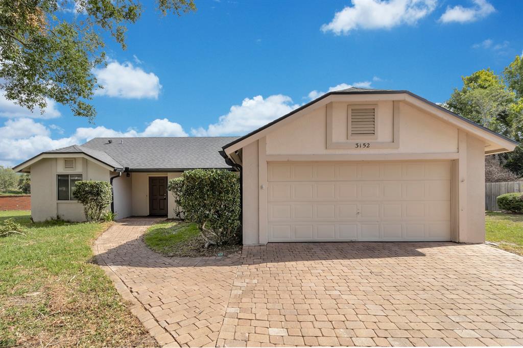 A single-story house with a beige exterior, a two-car garage, and a brick paver driveway — 3152 S HORIZON PLACE, OVIEDO, FL