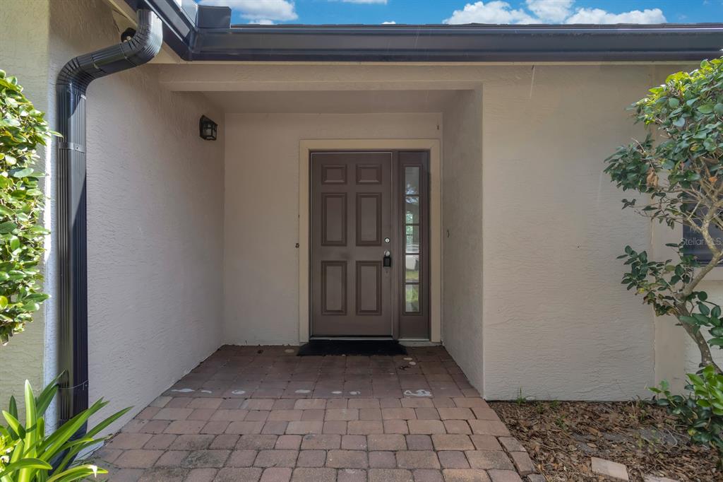 A brown front door with a side window sits under a covered entryway with pavers — 3152 S HORIZON PLACE, OVIEDO, FL