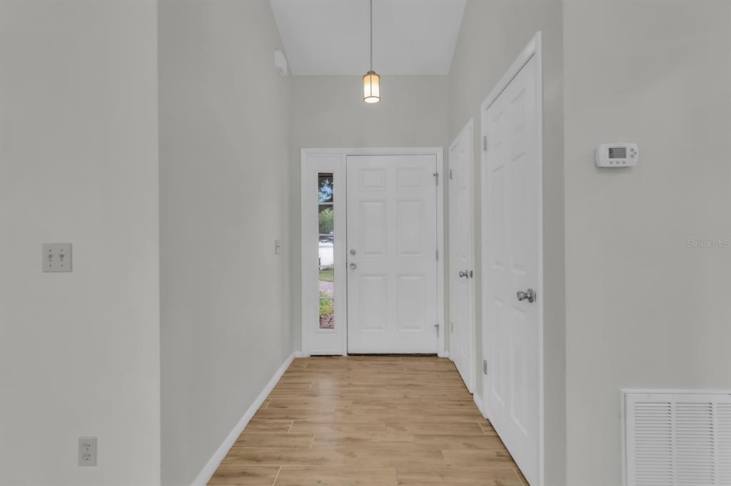 An entryway features light wood-look flooring, white walls, a white front door, and a pendant light — 3152 S HORIZON PLACE, OVIEDO, FL