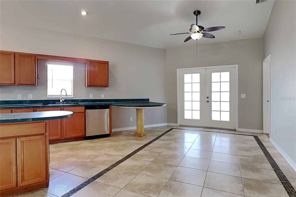 A kitchen with wood cabinets, green countertops, and tile flooring leads to a glass door — 229 LOOKOUT DRIVE, APOLLO BEACH, FL