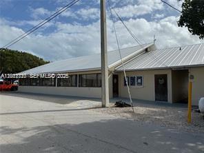 A low-slung, light-colored building with a metal roof stands beside a gravel parking area — 325 Calusa St, Key Largo FL 33037, KEY LARGO, FL