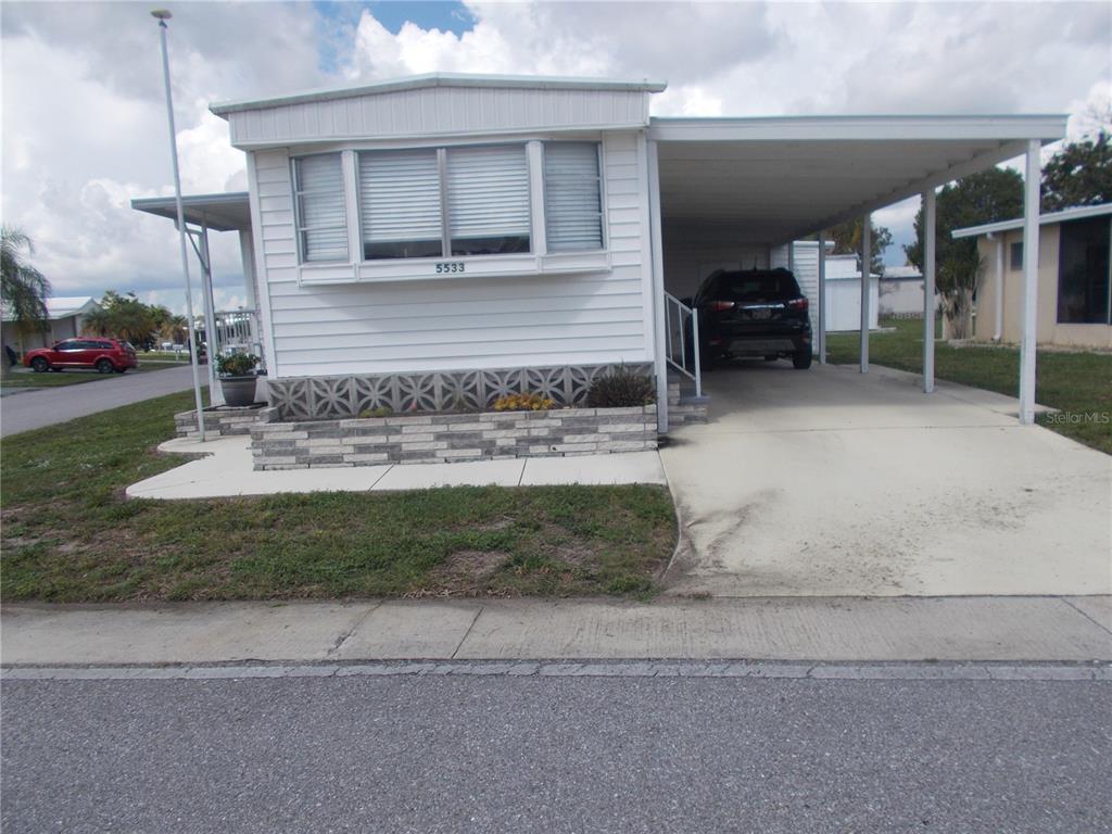 A white mobile home features a carport, a concrete driveway, and a decorative stone planter — 5533 HOLIDAY PARK BOULEVARD, NORTH PORT, FL