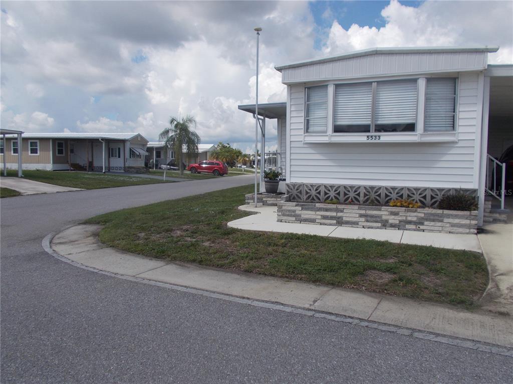 A white mobile home with a decorative block skirting sits on a corner lot — 5533 HOLIDAY PARK BOULEVARD, NORTH PORT, FL