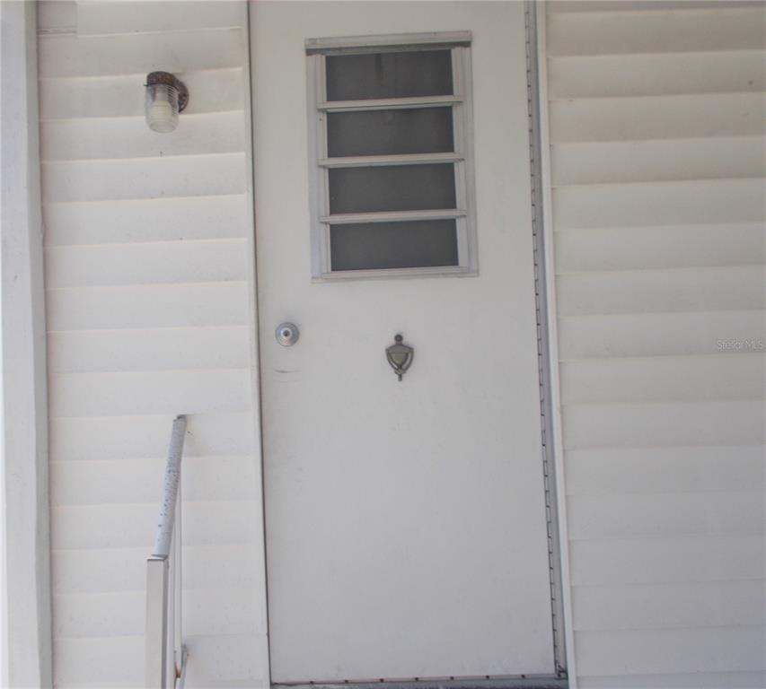 A white exterior door with a small window and a metal handrail on the left — 5533 HOLIDAY PARK BOULEVARD, NORTH PORT, FL