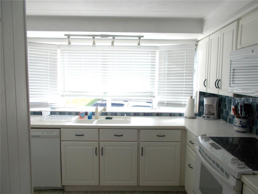A kitchen features white cabinets, a double sink, a bay window, and blue tile backsplash — 5533 HOLIDAY PARK BOULEVARD, NORTH PORT, FL