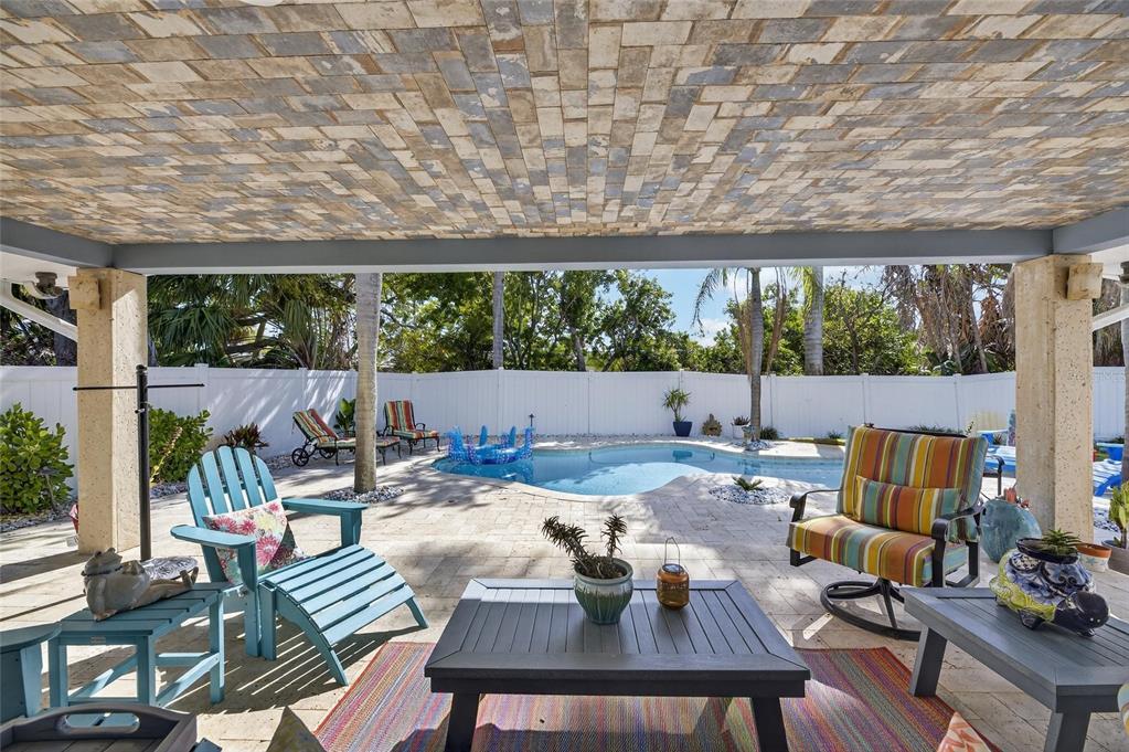 A covered patio features a brick-patterned ceiling, stone flooring, and a view of a swimming pool — 931 GULF BOULEVARD, BELLEAIR BEACH, FL
