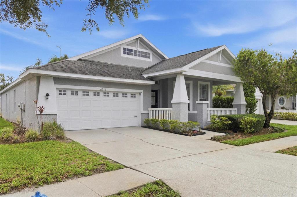 A single-story house with a gray stucco exterior, a two-car garage, and a front porch — 4613 CORSAGE DRIVE, LUTZ, FL