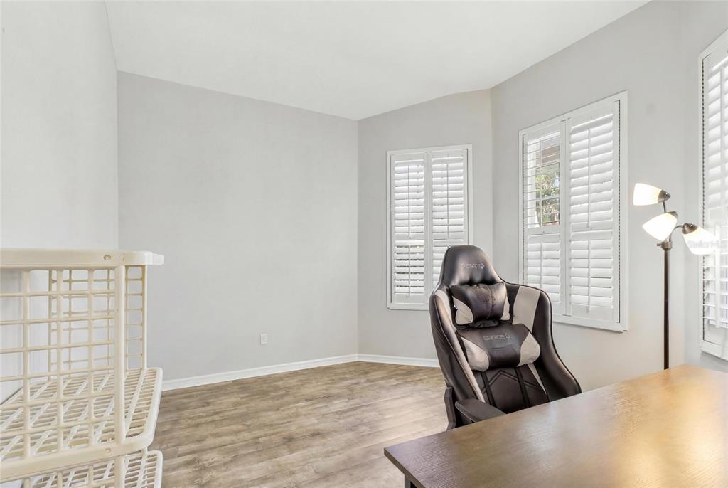 A home office features wood-look flooring, plantation shutters, a gaming chair, and a desk — 4613 CORSAGE DRIVE, LUTZ, FL