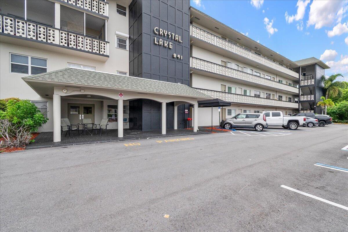 The exterior of a multi-story apartment building features a covered entrance and parking lot — 941 Crystal Lake Drive # 402, Deerfield Beach FL 33064, DEERFIELD BEACH, FL