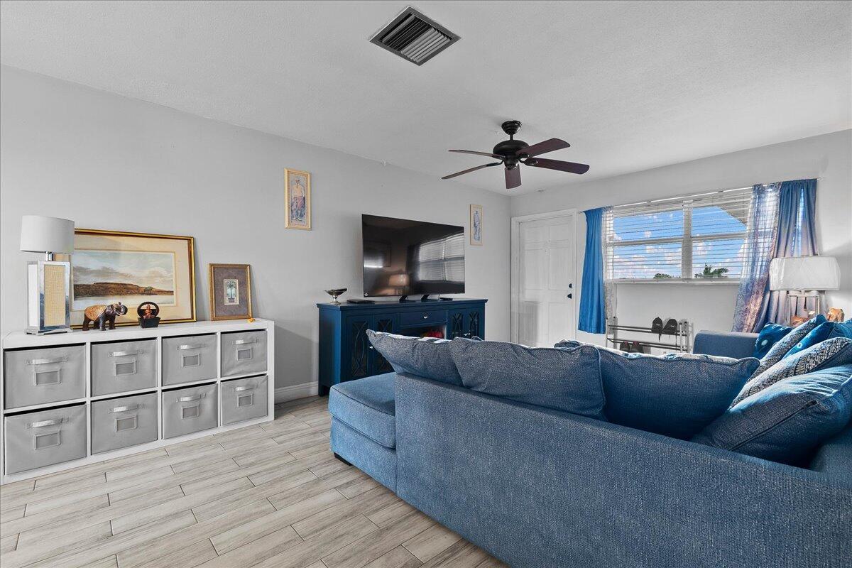 A living room features a blue sectional sofa, a white storage unit, and wood-look flooring — 941 Crystal Lake Drive # 402, Deerfield Beach FL 33064, DEERFIELD BEACH, FL